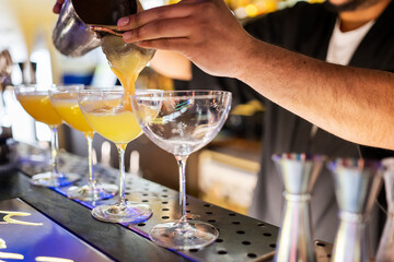 A bartender pours a yellow cocktail through a strainer into coupe glasses, showcasing professional...