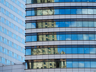 Reflective blue glass facade of modern office building capturing cloud reflections with geometric pattern