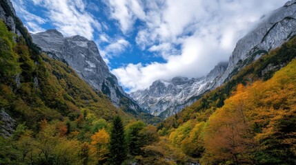 Obraz premium Majestic mountain valley in autumn, showcasing vibrant foliage against towering, snow-dusted peaks under a partly cloudy sky. : Generative AI