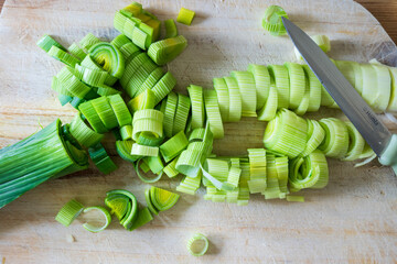 cutting green leek with a knife on a wooden board - vegetable preparation concept