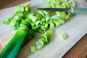 cutting green leek with a knife on a wooden board - vegetable preparation concept