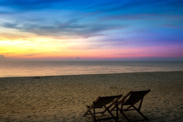 A serene beach at sunset with a vibrant sky of yellow, pink, and purple hues, featuring a lone chair on the golden sand and a calm sea, perfect for relaxation. Krabi Thailand