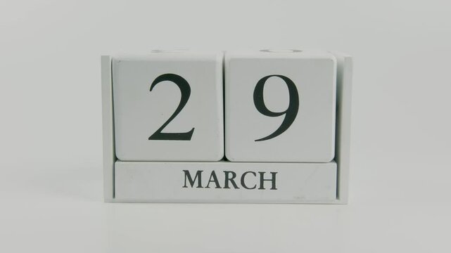 A hand flips a wooden calendar from March 29th to March 30th on a white background, symbolizing the quick passage of time and the change of days