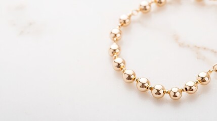 Obraz premium Elegant gold bead necklace resting on a smooth, white marble surface.