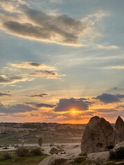 A beautiful sunset casts a warm glow over the distinctive rock formations in Goreme, Cappadocia. The sky is filled with vibrant colors, creating a breathtaking view of nature's beauty
