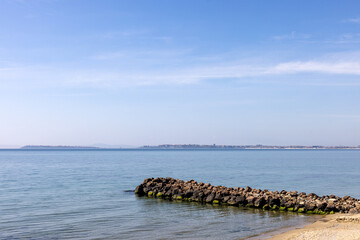 Rocky breakwater by calm sea with distant coastline in Burgas, Bulgaria.
