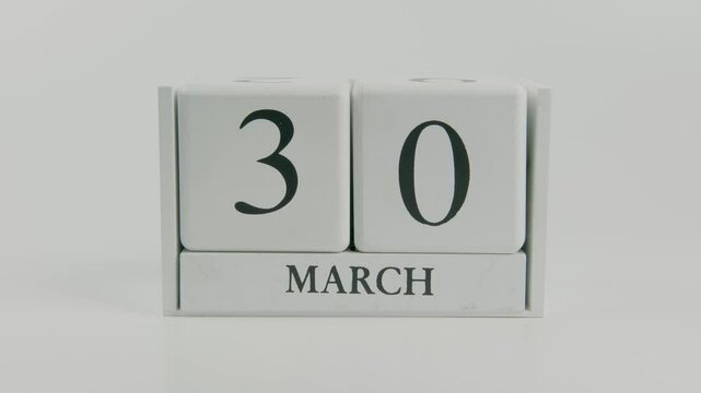 A hand flips a wooden calendar from March 30th to March 31st on a white background, symbolizing the transition to the end of the month and the arrival of a new day