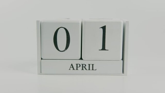 A hand flips a wooden calendar from April 1st to April 2nd on a white background, symbolizing the passage of time and the arrival of a new day
