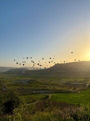 Brightly colored hot air balloons float above the unique rock formations and lush valleys of Goreme, Cappadocia, creating a breathtaking view at sunrise