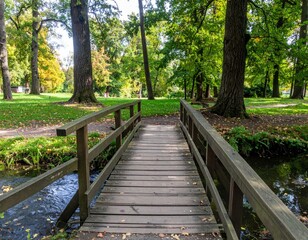 Fototapeta premium Peaceful Wooden Bridge Over Stream in Lush Green Park Landscape