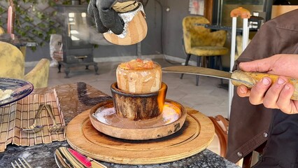 A chef skillfully removes the lid from a clay pot containing a pottery kebab at a restaurant in Goreme, Cappadocia, showcasing local cuisine and dining culture