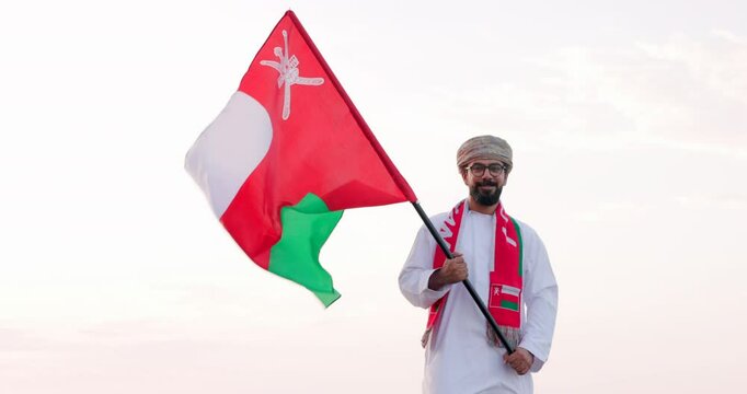 Omani man stands with Omani National Flag, wearing omani traditional dishdasha and Musaar