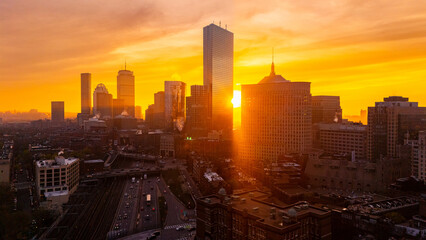 Obraz premium Golden hour in the lively modern city. Setting sun hides behind the towers of Boston, Massachusetts, USA. Orange sky at backdrop. Aerial view.