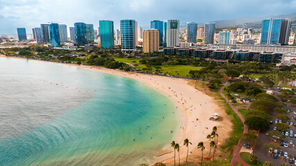 Naklejka premium Beautiful sandy beach surrounded by green park. Modern high-rise buildings of Waikiki at backdrop. Hawaii, USA.