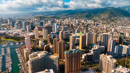 Fototapeta premium Architecture of Honolulu, Hawaii, USA lit with bright sun. Massive white cloudscape gathered above the mountains. Aerial view.