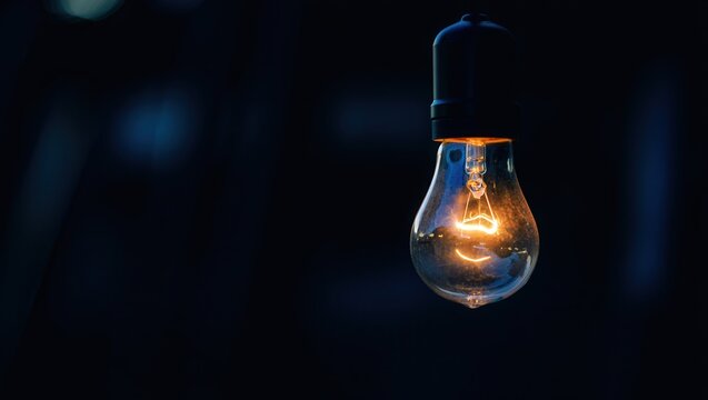 A single lit light bulb hanging from a string in darkness.