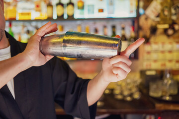 A bartender skillfully shakes a cocktail shaker in a lively bar setting, surrounded by bottles of...