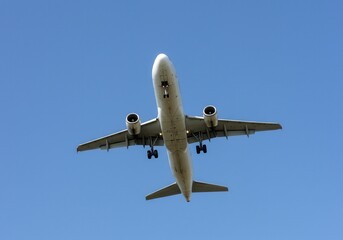 Fototapeta premium Airplane with landing gear down flies overhead against a clear blue sky during the daytime