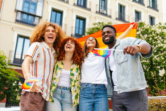 Happy multi ethnic friends celebrating gay pride holding rainbow flag and laughing - Powered by Adobe