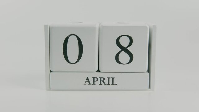 A hand flips a wooden calendar from April 8th to April 9th on a white background, symbolizing the transition between days with a clean and minimal style