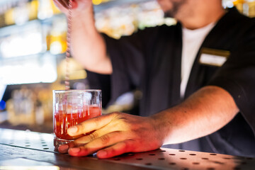 A bartender skillfully stirs a vibrant cocktail with a metal stirrer, highlighting the artistry of drink preparation in a lively bar setting. Close-up view with focus on motion and ingredients.