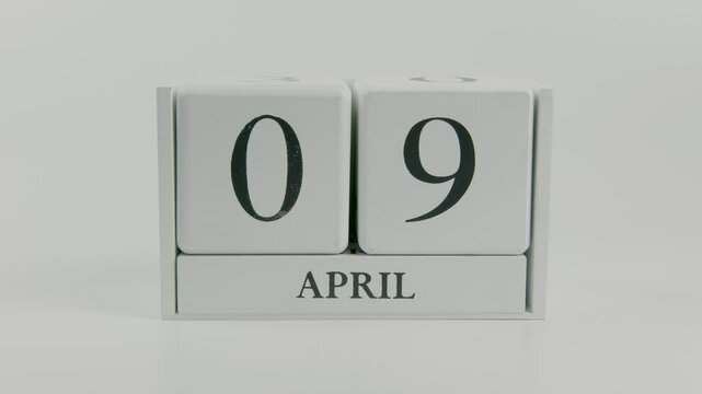 A hand flips a wooden calendar from April 9th to April 10th on a white background, showing the shift from one day to the next with a simple focus on time