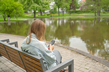 Woman on Bench by Lake Using Smartphone in Park