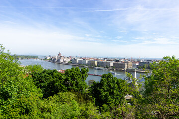 Panoramic view of Budapest city with Parliament building, Danube River, bridges and green trees under clear blue sky