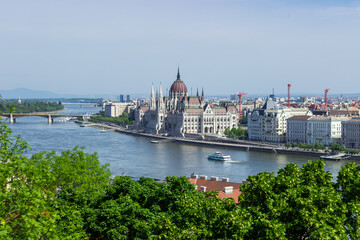 Panoramic view of Budapest city with Parliament building, Danube River, bridges and green trees under clear blue sky