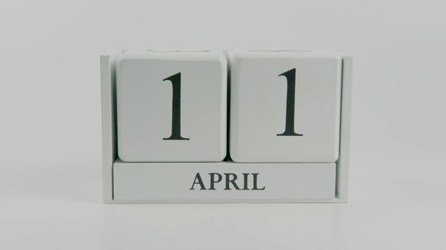 A hand flips a wooden calendar from April 11th to April 12th on a white background, representing the natural passage of time from one day to the next