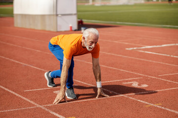 An old athlete in starting position on stadium.