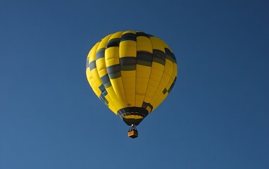 Yellow and Blue Hot Air Balloon Soaring High in a Clear Blue Sky