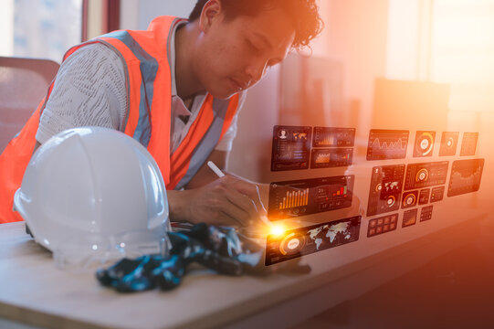 Engineering man wearing orange vest sitting in office hard hat on table using pen working on digital tablet analysing data charts on virtual screen