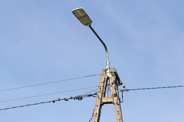 Old street lamp metal structure. Electrical wires on blue sky background. Urban utility pole...