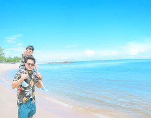 Father and Son Beach Day: A heartwarming scene of a father carrying his son on his shoulders along a picturesque beach, capturing a moment of joy, adventure.
