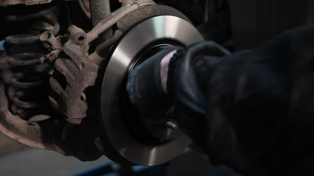 Mechanic Installing New Brake Disc on Car Wheel Hub Close-up of a mechanic&rsquo;s gloved hands mounting a shiny new brake disc onto a vehicles