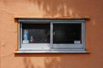 Small rectangular, figured glass window set into stucco textured orange wall. Surrounding trees create a yin-yang type contrasting shadow, adding zen-like tranquility and simplicity to everyday life.
