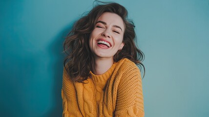 Obraz premium Close-Up Portrait of Young Woman in Mustard Yellow Chunky Knit Sweater, Joyful Expression with Closed Eyes and Open-Mouthed Laugh Against Solid Turquoise Blue Background