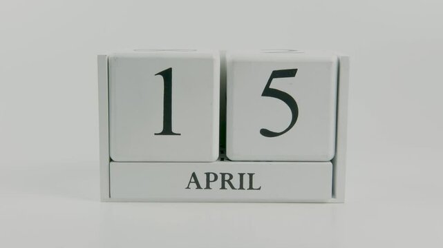 A hand flips a wooden calendar from April 15th to April 16th on a white background, symbolizing the passage of time and the importance of daily planning and organization
