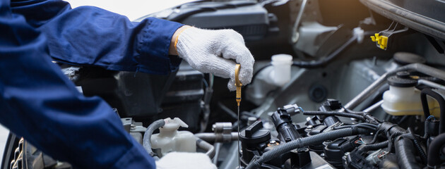 Close-up shot mechanician checking engine lubricant oil level at auto service station.