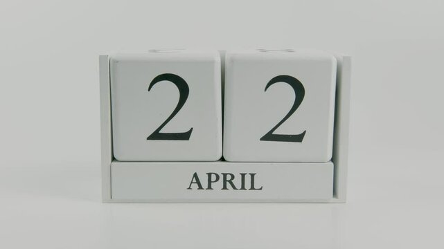 A hand flips a wooden calendar from April 22nd to April 23rd on a white background, symbolizing the passage of time, and highlighting the ongoing journey of daily tasks and responsibilities