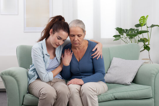 Granddaughter hugs and comforts her elderly grandmother in a moment of sadness. Emotional family scene showing love, and support during a difficult time, disease pain, or family bereavement