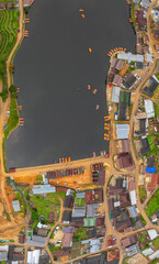 Naklejka premium aerial top view of a lakeside village, showcasing a mix of rustic architecture, lush greenery, and boats scattered across the calm water. A harmonious blend of natural beauty and human settlement..