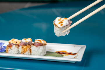 hand with wooden chopsticks taking sushi roll on a deep blue background. Asian restaurant menu. Copy space