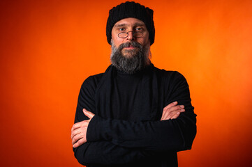 Portrait of a confident mature man with arms crossed in front of him, wearing a cap and glasses on...
