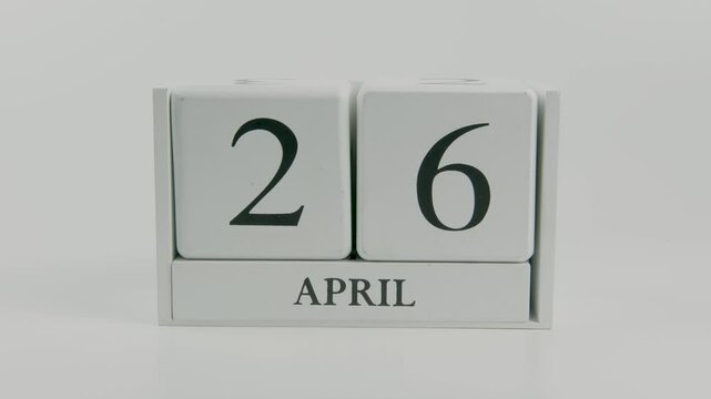 A hand flips a wooden calendar from April 26th to April 27th, marking the transition of days on a white background, emphasizing the flow of time