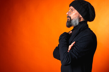 Portrait of stylish mature man with beard and glasses in black hat looking aside thoughtfully,...
