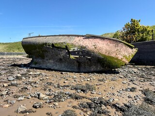 Decaying boat hull coated in moss and algae resting on rocks at low tide