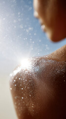 A close-up of a glistening shoulder of a woman with medium brown skin, showcasing droplets of water sparkling in the sunlight against a soft background