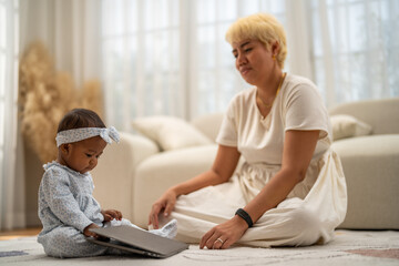Mother sitting on floor watching her baby explore laptop enjoying quality family time at home, representing modern parenting, digital lifestyle of working mom and early childhood development bonding